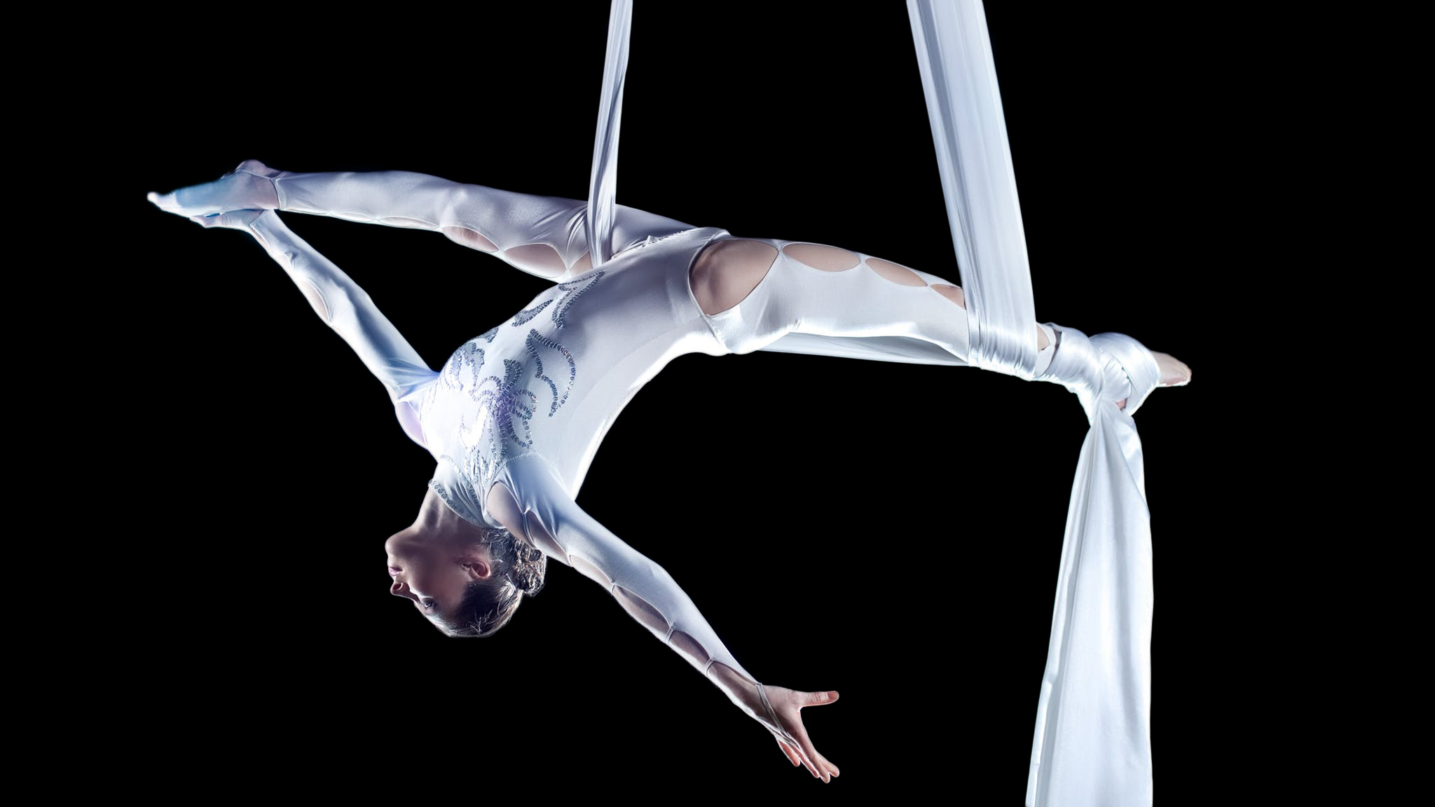A beautiful acrobat in white performing a routine on silks